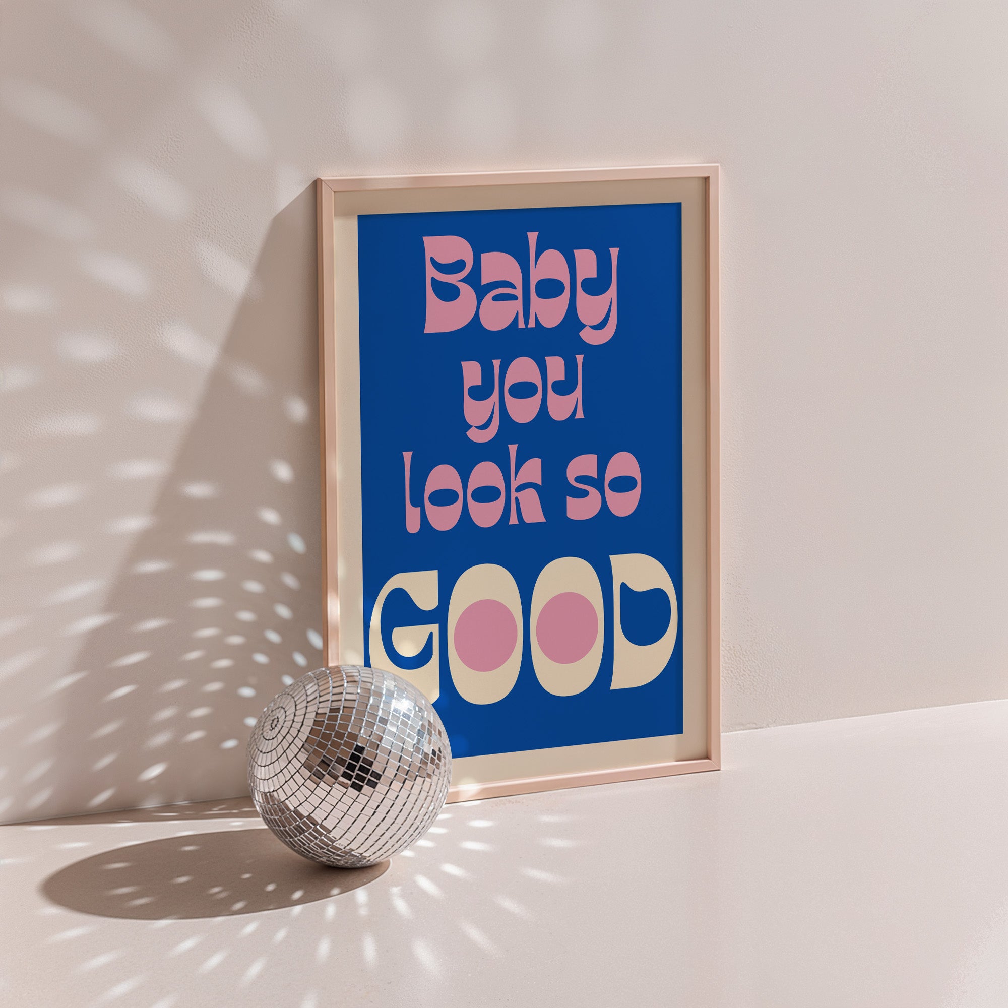 Baby You Look So Good poster in wood frame beside a disco ball, pink and cream bubble lettering on cobalt