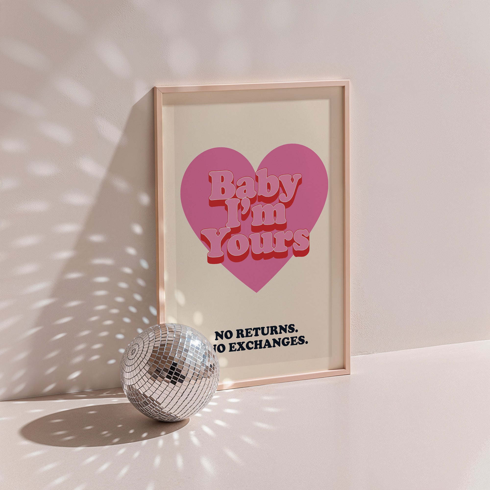 Baby I'm Yours poster in wood frame beside a disco ball, red heart with 'no returns no exchanges' caption on navy