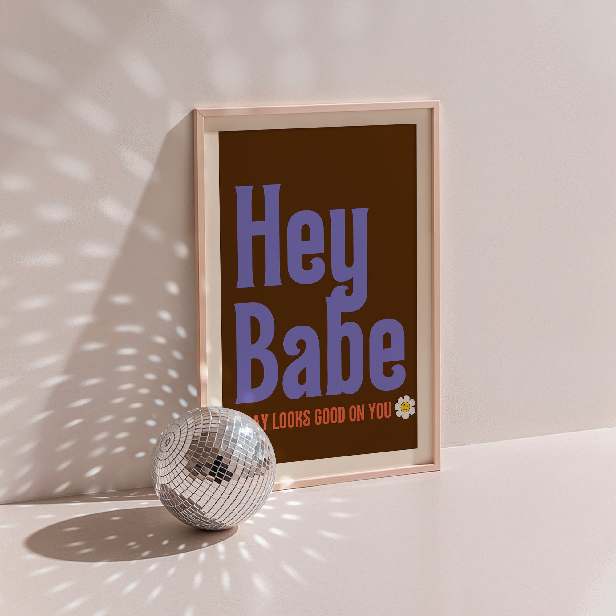Hey Babe poster in wood frame beside a disco ball, purple retro lettering with daisy on chocolate brown