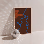 Don't Say Goodnight Yet poster in wood frame beside a disco ball, blue line-drawn faces with orange lettering on brown