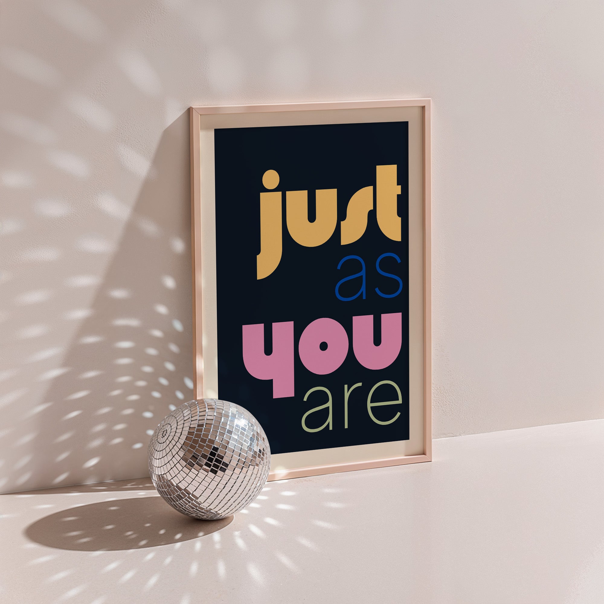 Just As You Are poster in wood frame beside a disco ball, multicoloured lettering on black