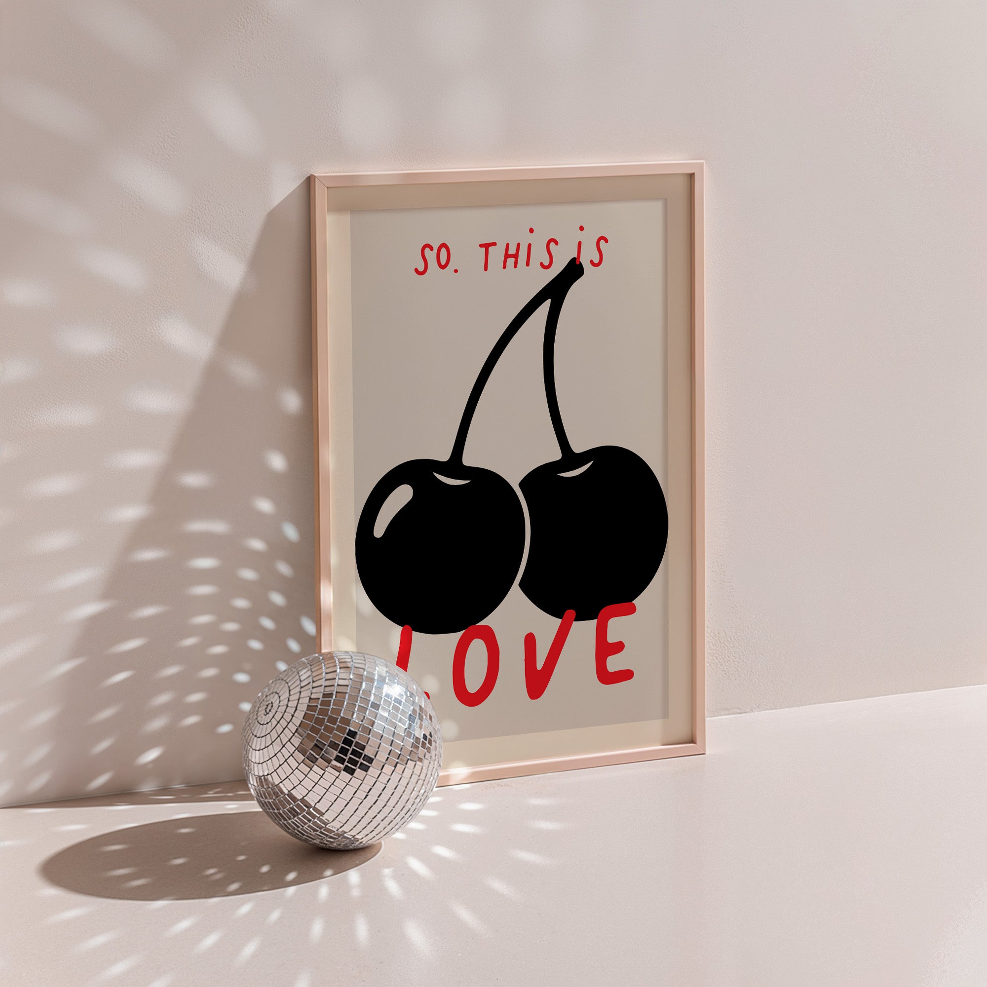 So. This Is Love poster in wood frame beside a disco ball, black cherries with red hand lettering on cream