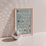 Little Magic poster in wood frame beside a disco ball, cream lettering with coloured stars on blue-grey