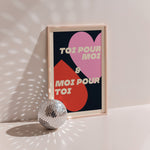 Toi Pour Moi & Moi Pour Toi poster in wood frame beside a disco ball, pink and red hearts with cream lettering on navy