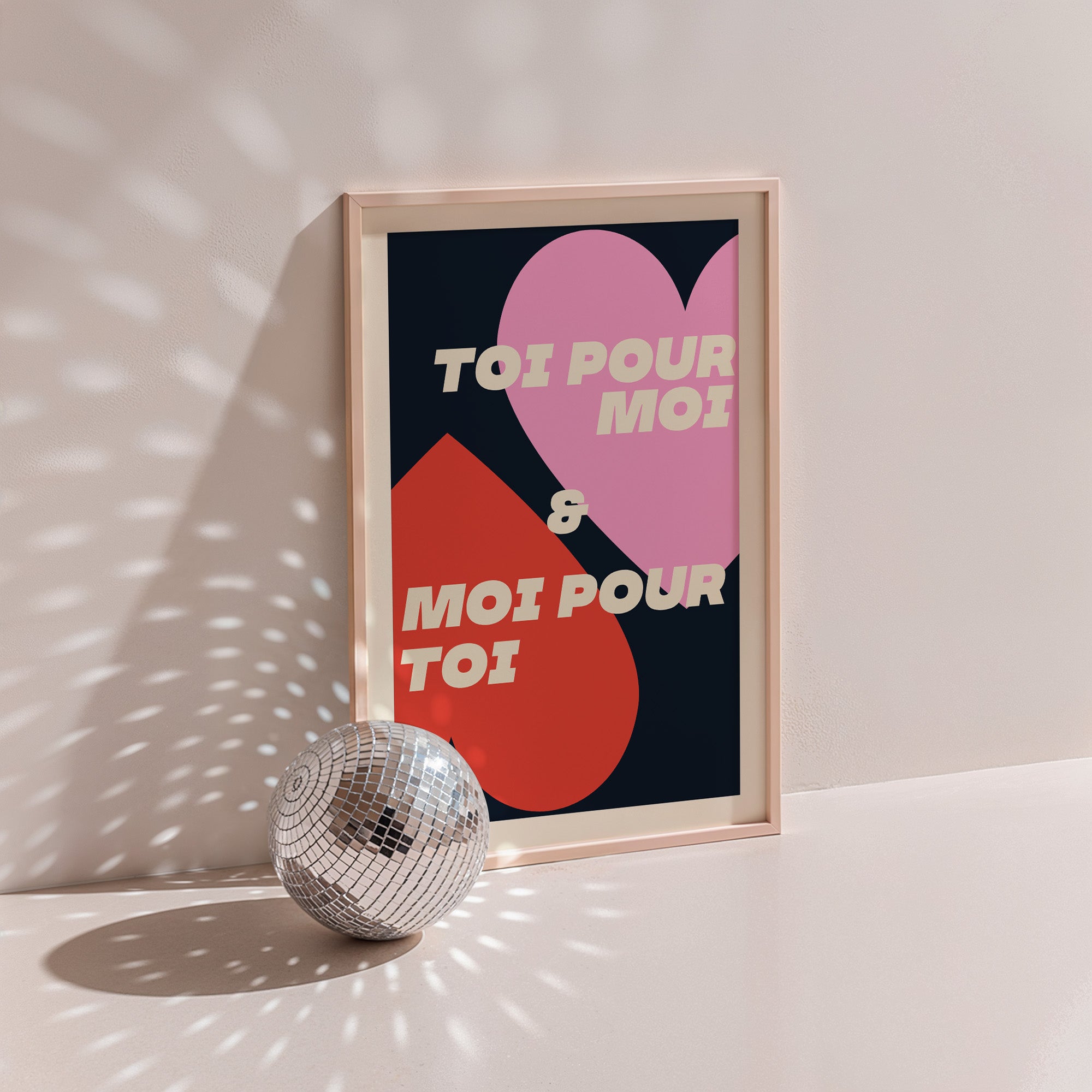 Toi Pour Moi & Moi Pour Toi poster in wood frame beside a disco ball, pink and red hearts with cream lettering on navy