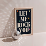 Let Me Rock You poster in wood frame beside a disco ball, cream serif lettering with multicoloured stars on navy