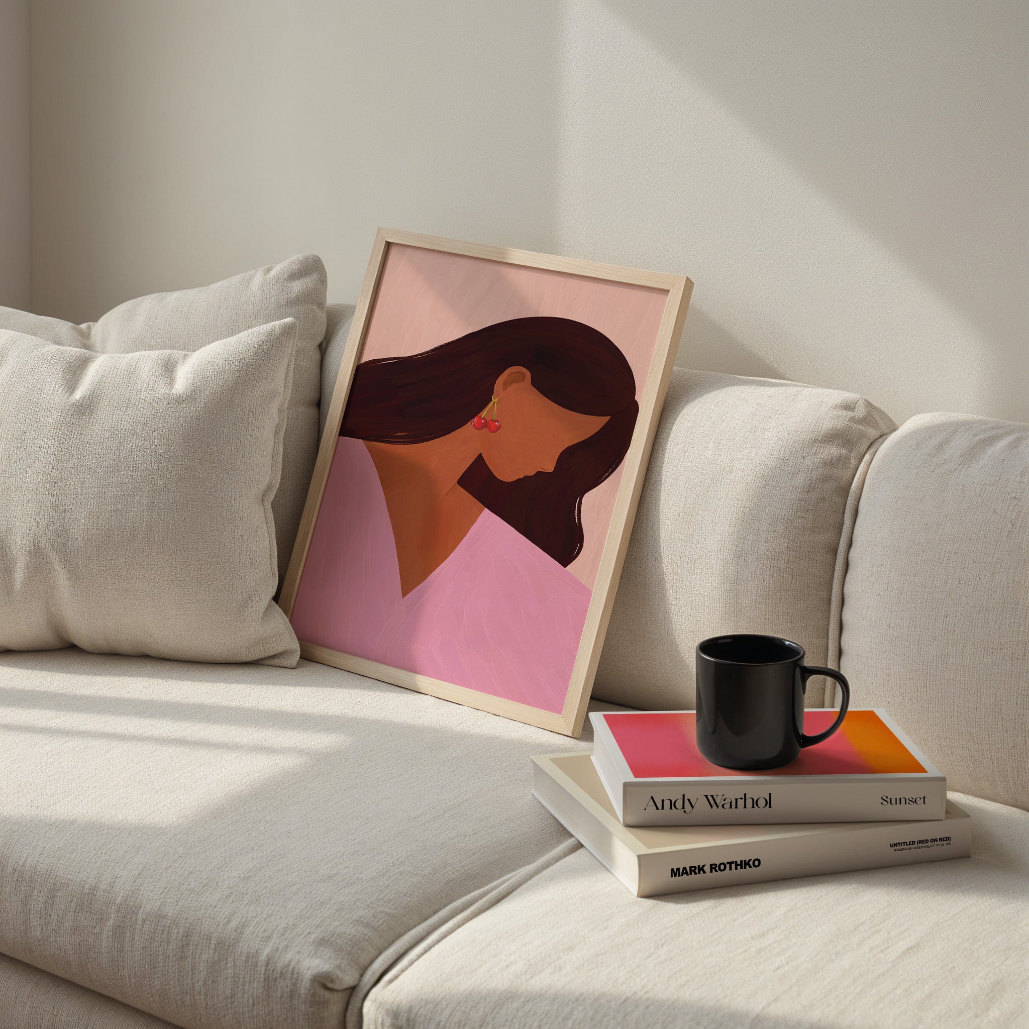 Framed artwork of a woman's face on a sofa with books and a mug.