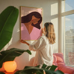 Woman admiring a framed artwork in a bright room with large windows.