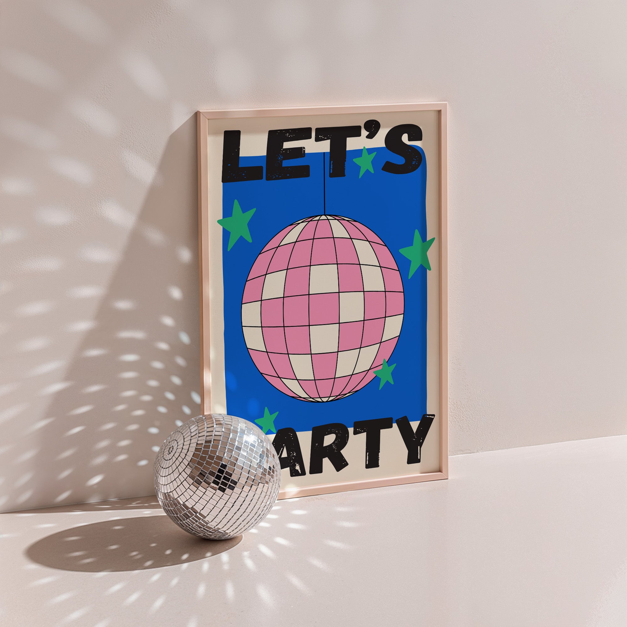 Let's Party poster in wood frame beside a disco ball, pink checkered disco ball with green stars on cobalt