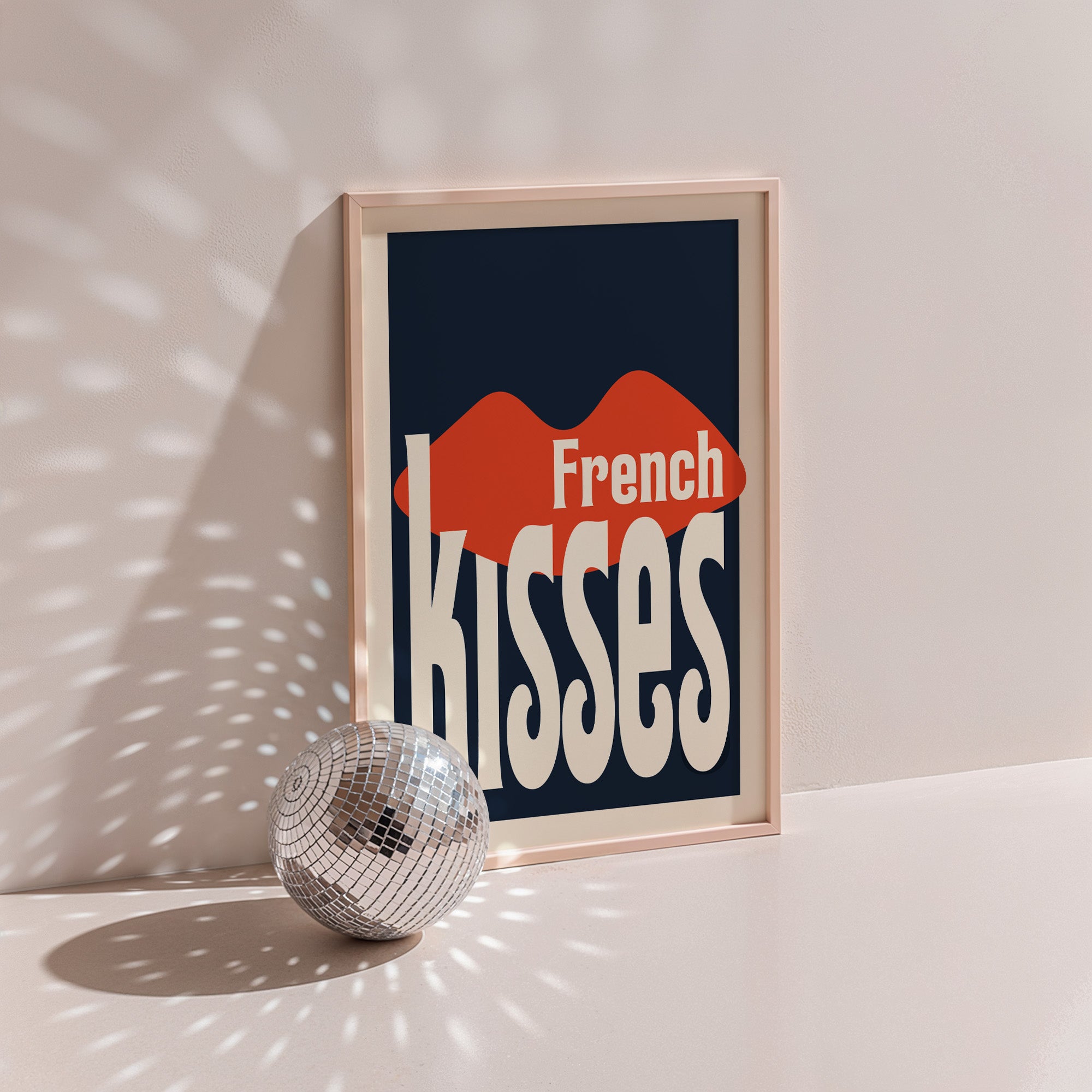French Kisses poster in wood frame beside a disco ball, red lips with cream warped lettering on navy