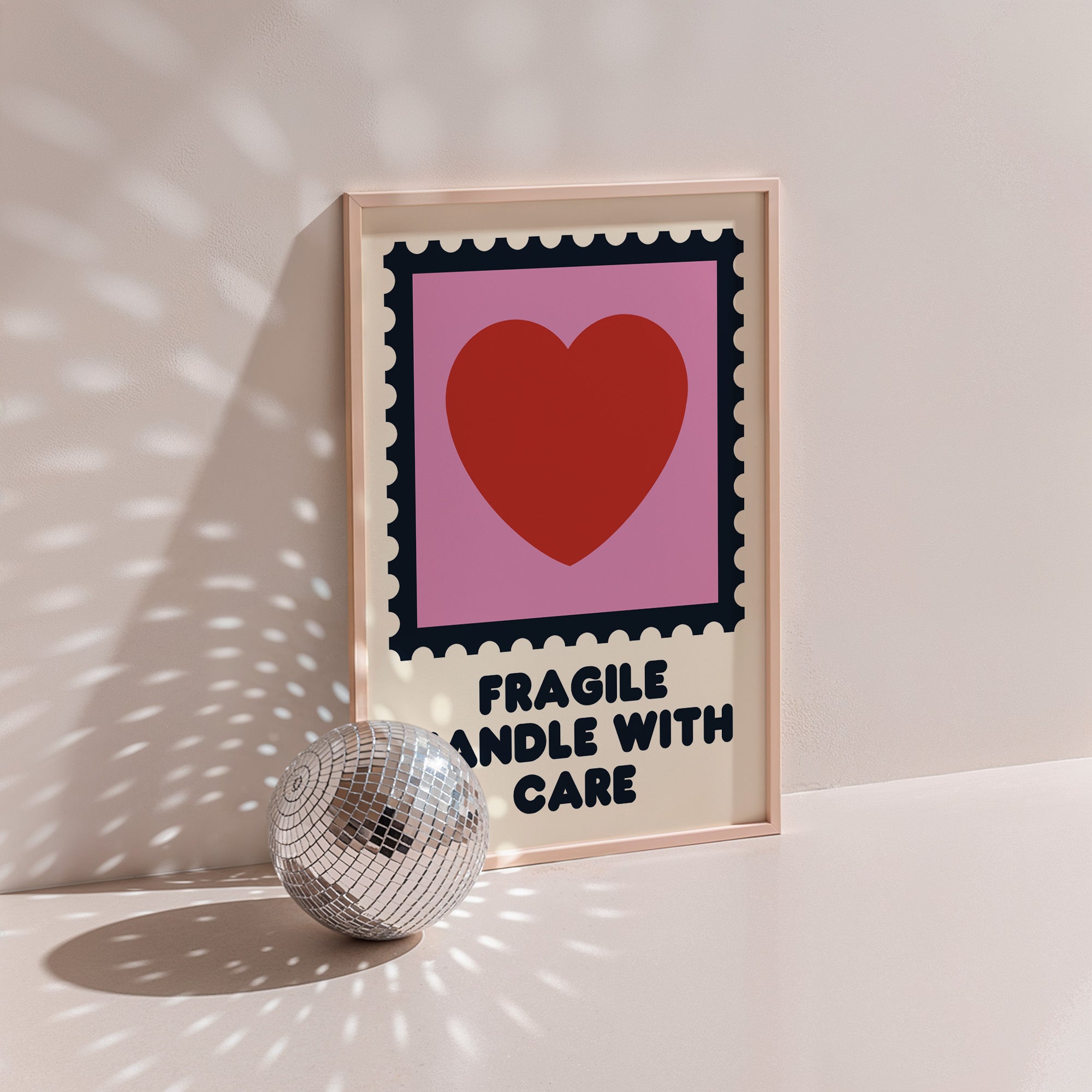 Fragile Handle With Care poster in wood frame beside a disco ball, postage stamp frame with red heart on pink