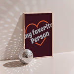 My Favorite Person poster in wood frame beside a disco ball, orange heart outline with grey lettering on burgundy