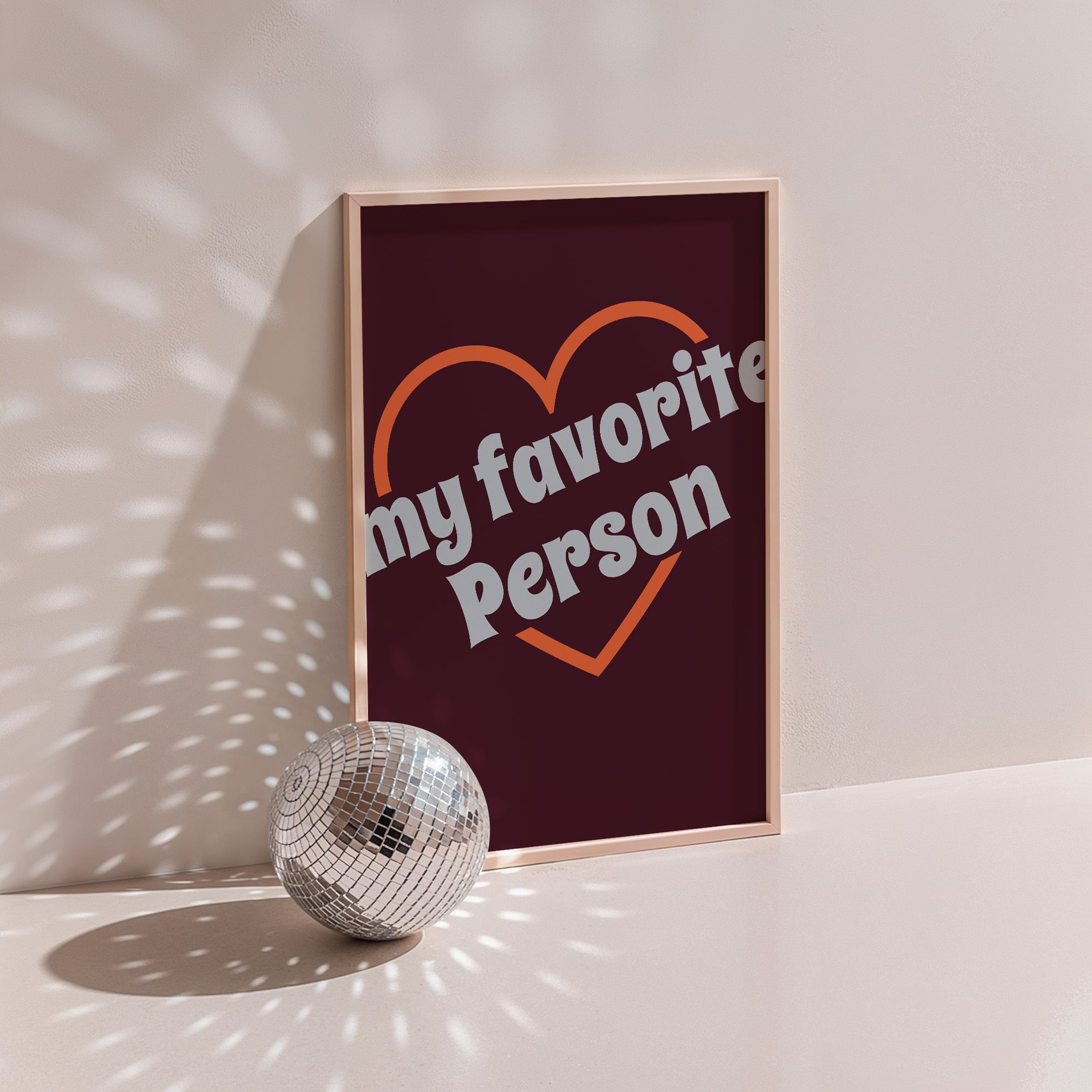 My Favorite Person poster in wood frame beside a disco ball, orange heart outline with grey lettering on burgundy