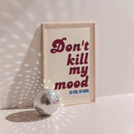Don't Kill My Mood poster in wood frame beside a disco ball, burgundy lettering on cream