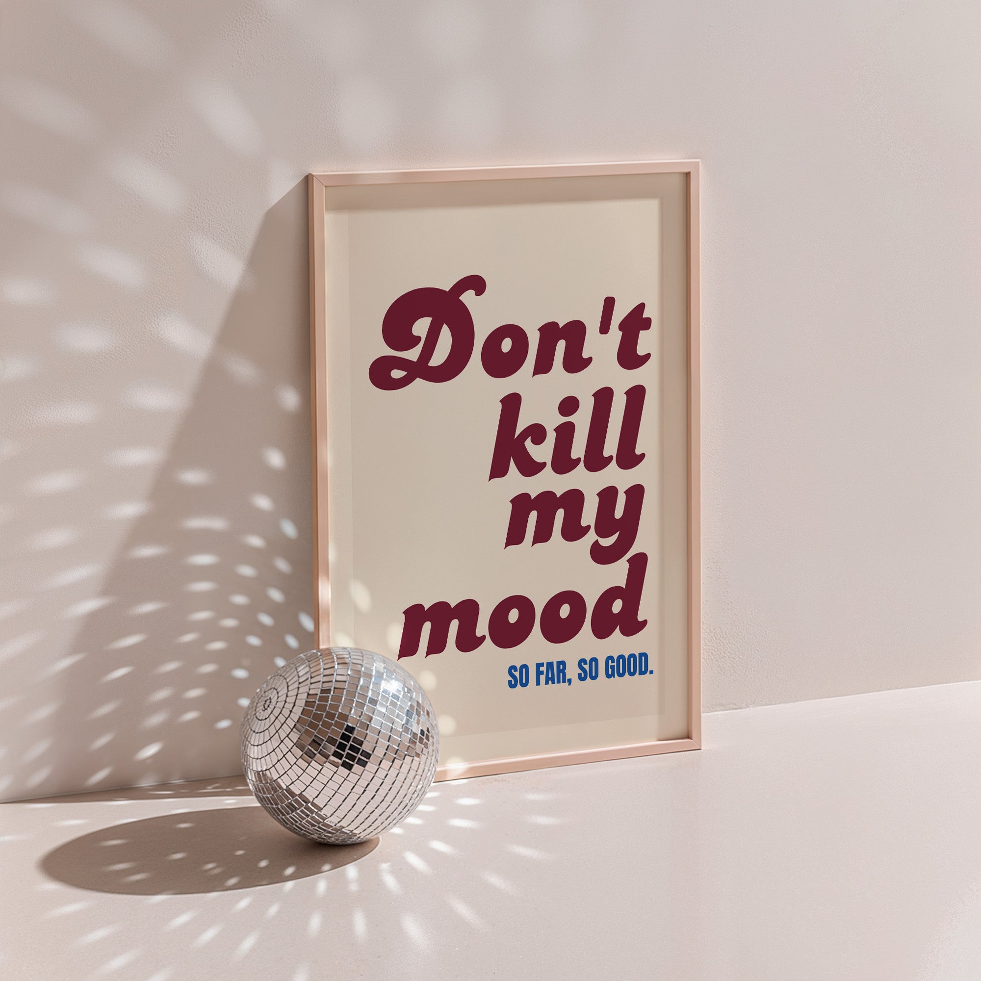 Don't Kill My Mood poster in wood frame beside a disco ball, burgundy lettering on cream