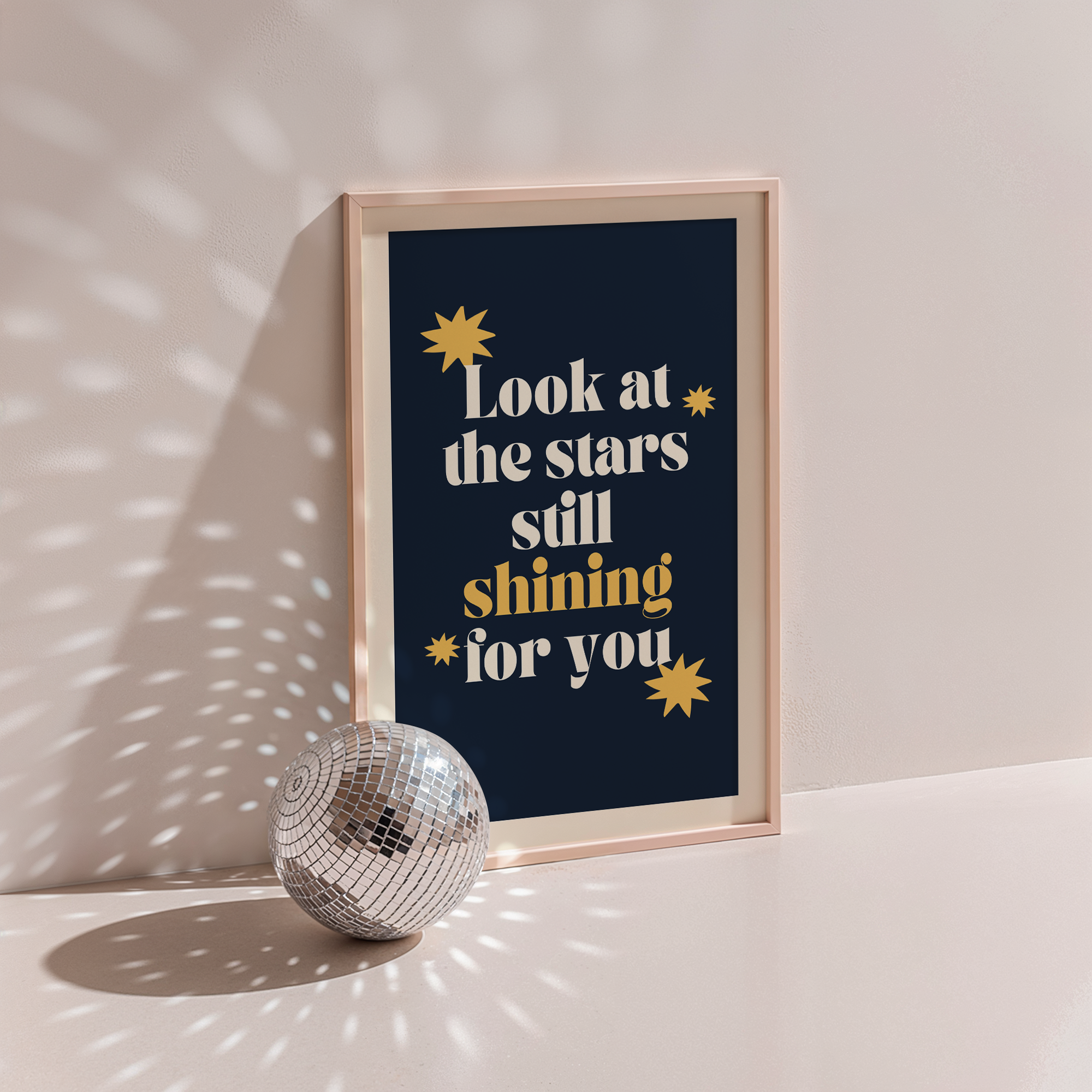 Look At The Stars poster in wood frame beside a disco ball, cream serif lettering with gold stars on navy