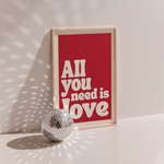 All You Need Is Love poster in wood frame beside a disco ball, red background with cream retro lettering