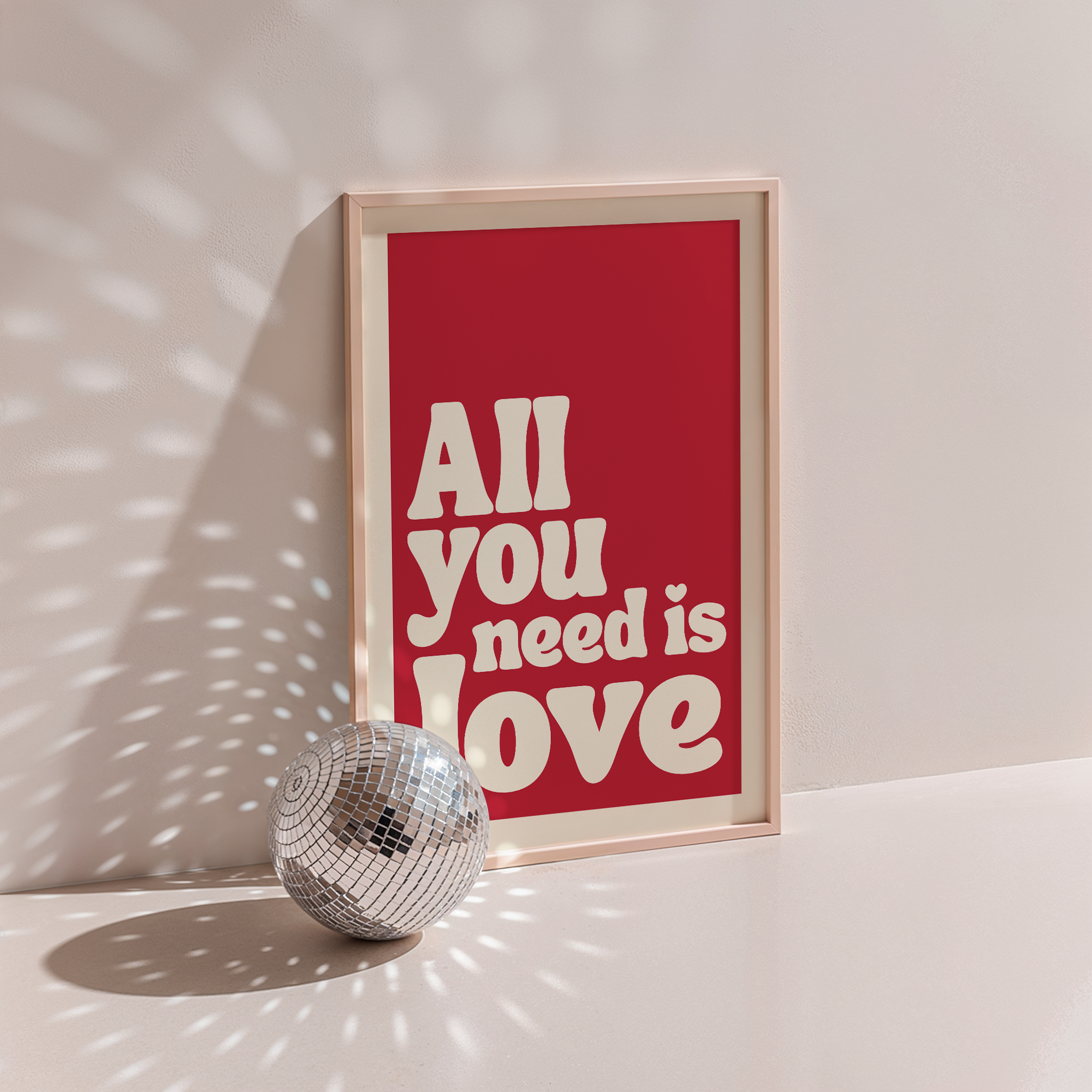 All You Need Is Love poster in wood frame beside a disco ball, red background with cream retro lettering