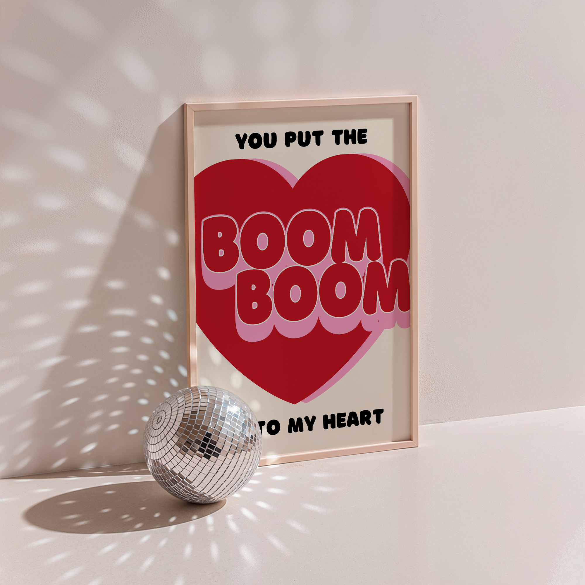 Boom Boom Into My Heart poster in wood frame beside a disco ball, red heart with bubble lettering on cream