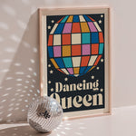 Dancing Queen poster in wood frame beside a disco ball, navy background with multicoloured disco ball